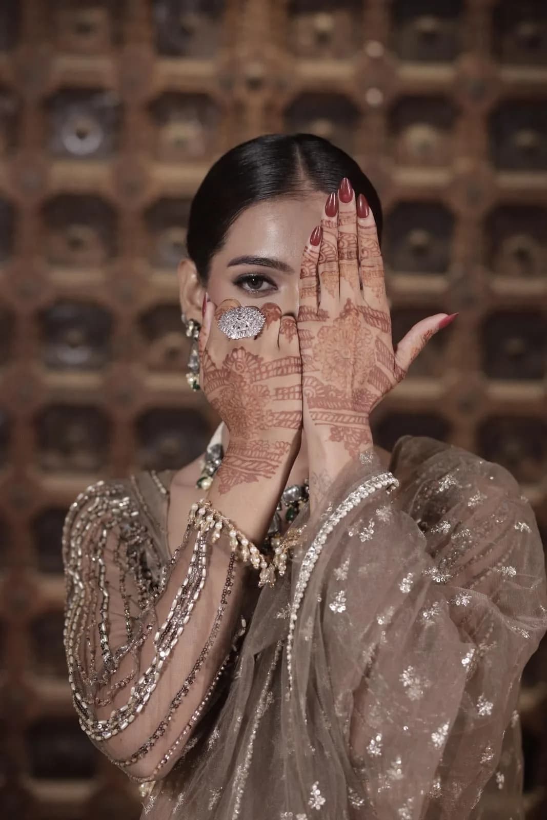Bride covering half her face with mehendi-covered hands, smoky eye showing