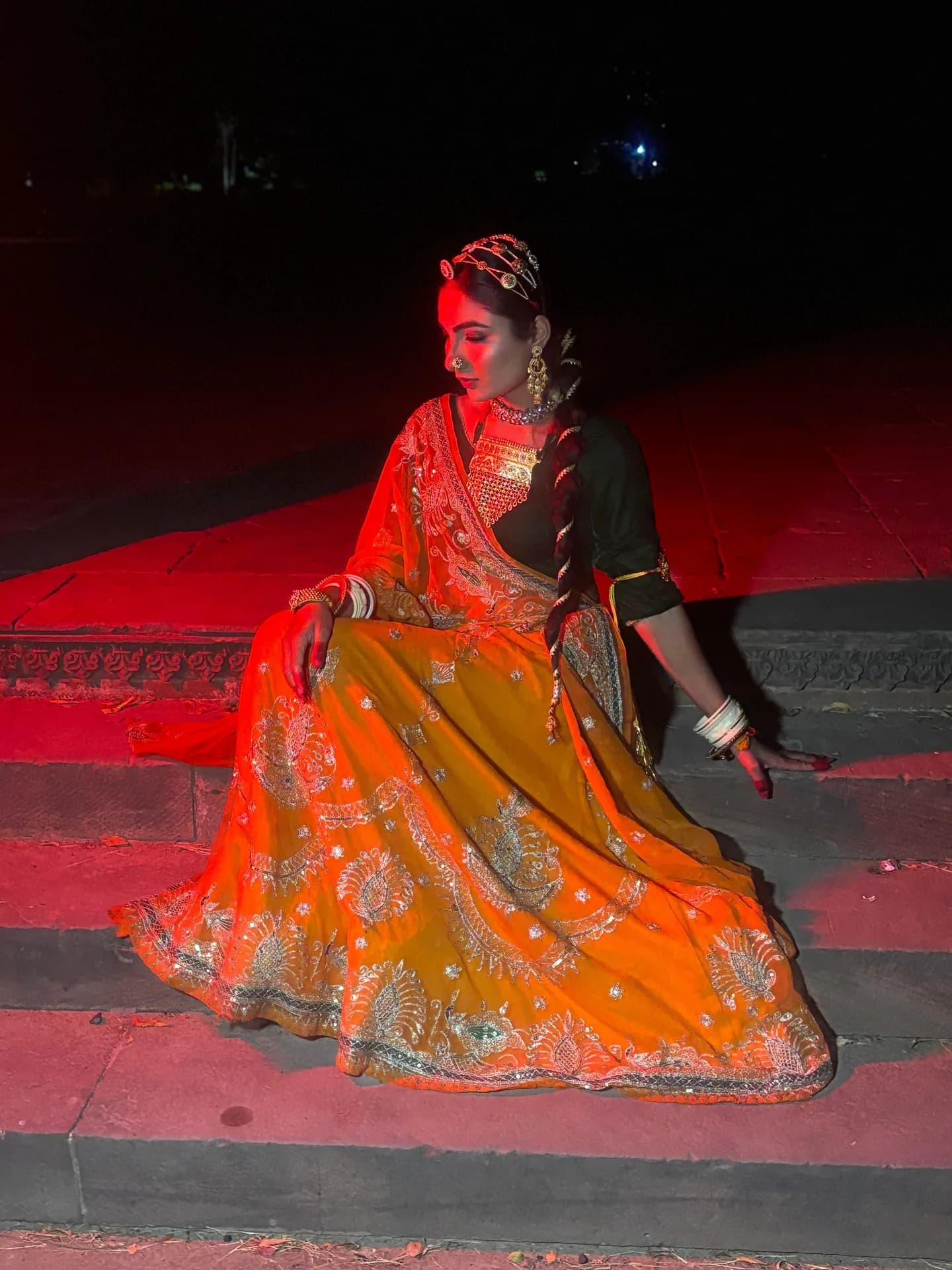 Seated editorial look in an orange lehenga under red light