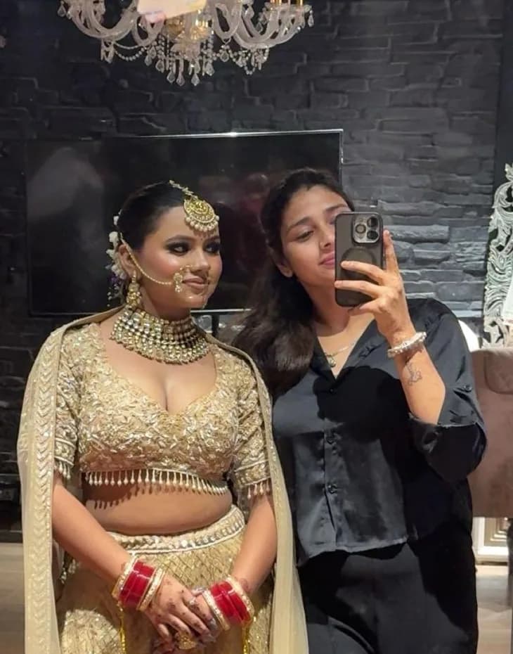 Bride in gold with her makeup artist, in the mirror after the final touch-up
